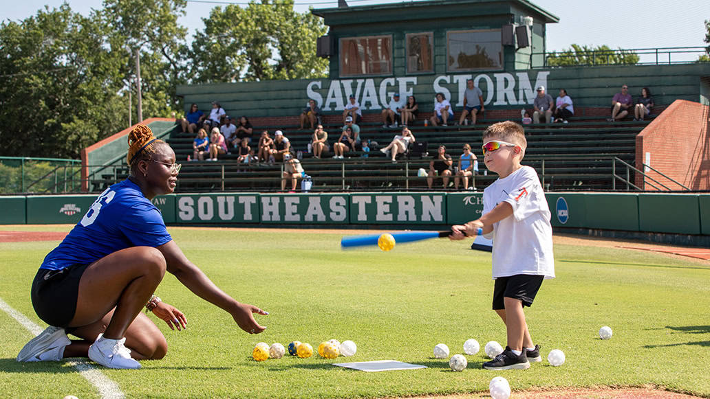 A coach pitches a ball to a young camper at the N7 Diamond Experience.
