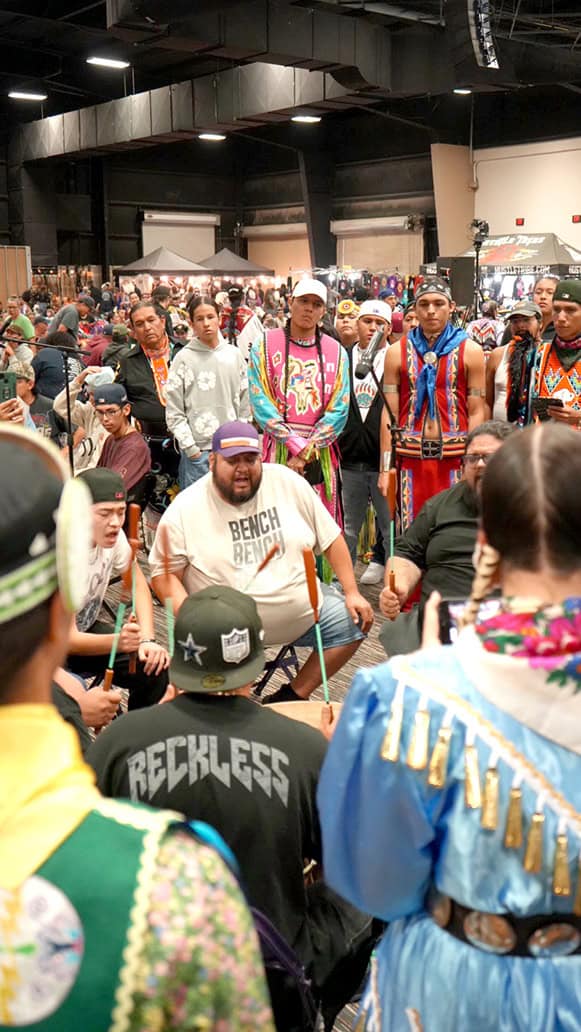 Onlookers stand behind the drum circle.