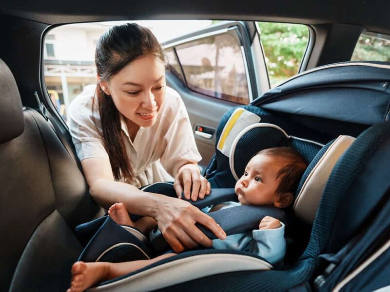 A mother buckles a baby into a car seat