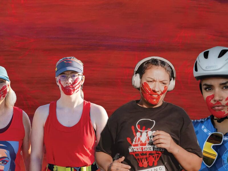 Four women stand together with red face paint on their mouths, representing MMIW