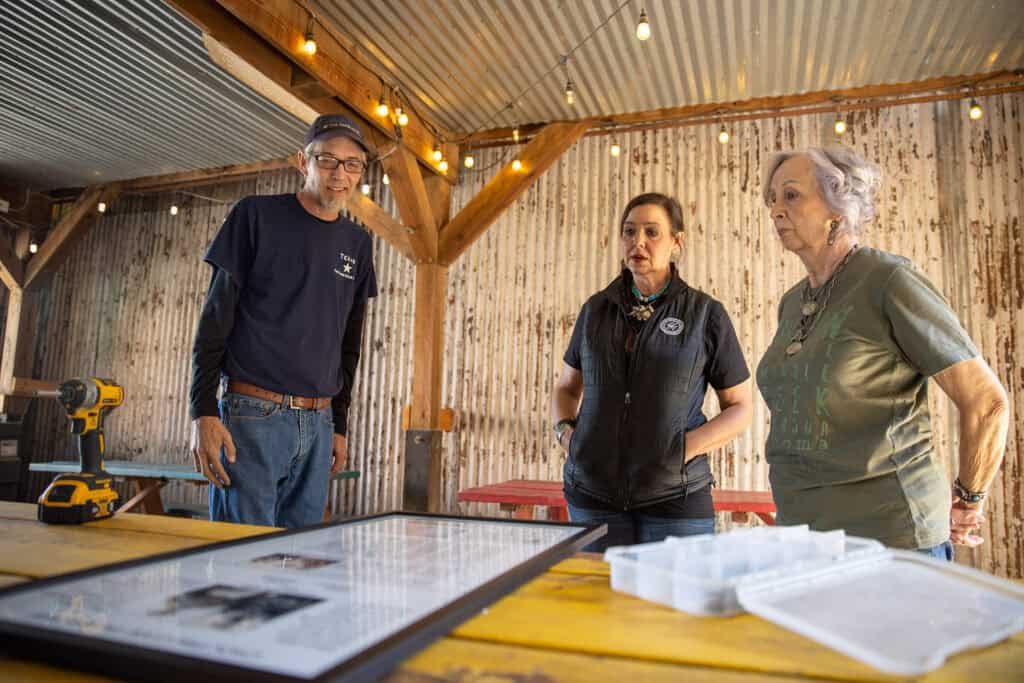 Three people look over items on display on a table.