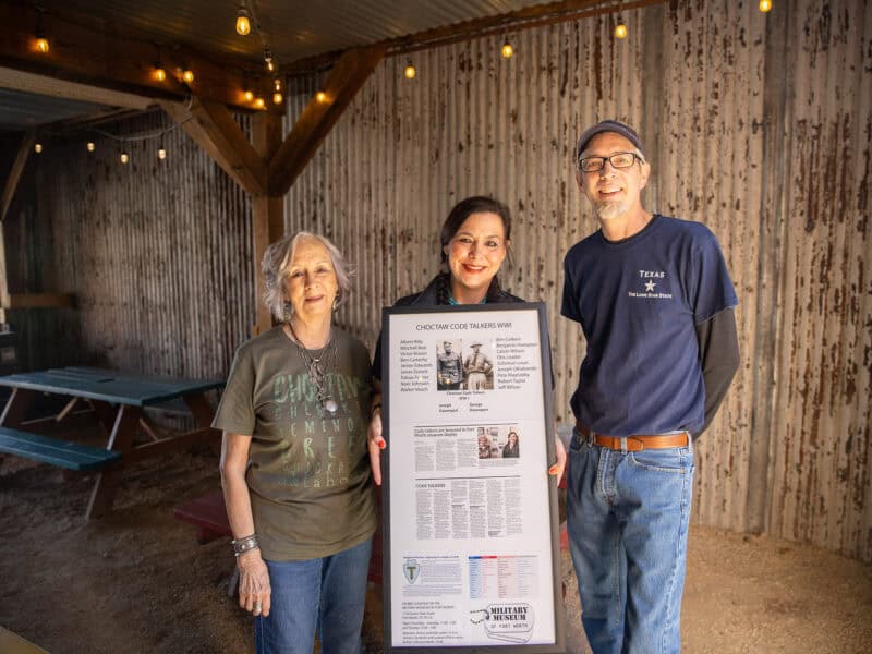Three people pose for a photo with a display about the Choctaw code talkers.