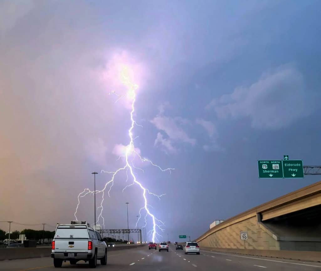 Lightning strikes in the distance as cars travel on the highway.