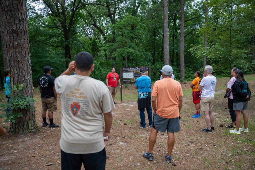 A group of people stand outside listening to a presentation.