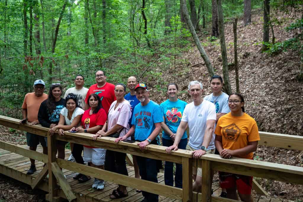 A group poses for a photo on a wooden bridge in the woods.