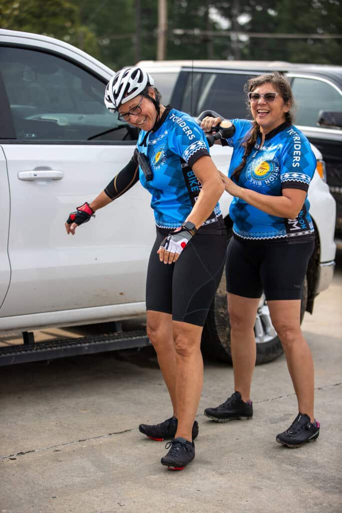 A woman uses a masage gun on a riders back.