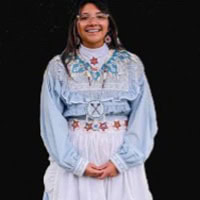 Young girl stands, smiling, wearing a light blue and white traditional dress.