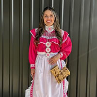 Young woman stands, holding a basket, wearing a hot pink and white traditional dress.