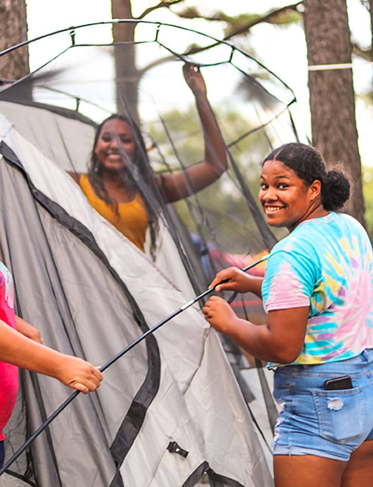 A young woman smiles at the camera whole setting up a tent.