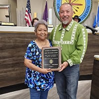 Woman in blue floral shirt stands with councilmember Anthony Dillard, holding a plaque.