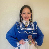 Young girl stands, smiling, wearing a blue and white traditional dress.