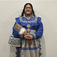 Young woman holds a feather and basket, wearing a blue and white traditional dress.