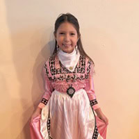 Young girl stands, smiling, in a pink and white traditional dress.