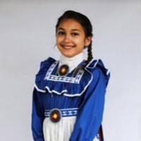Young girl stands, smiling, wearing a royal blue and white traditional dress.