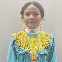Young girl wears a teal traditional dress and bright yellow beaded collar necklace.
