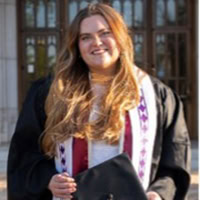 A woman poses for the camera wearing a graduation gown.