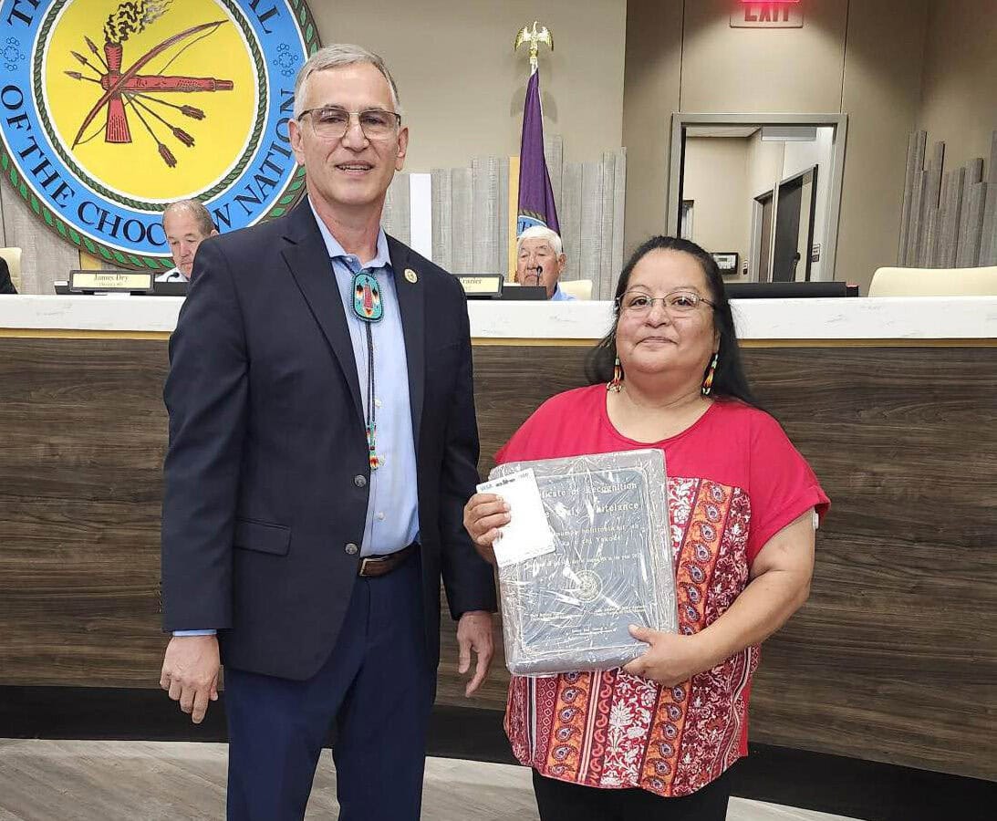 A man and a woman pose for a photo with the woman holding an award.