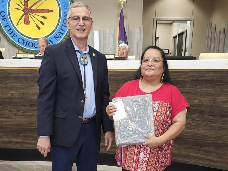 A man and a woman pose for a photo with the woman holding an award.