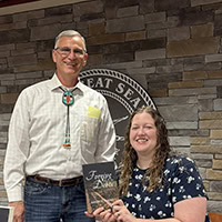 A man and a woman pose for the camera with the woman holding a book.