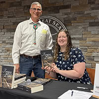 A man and a woman pose for the camera with the woman holding a book.