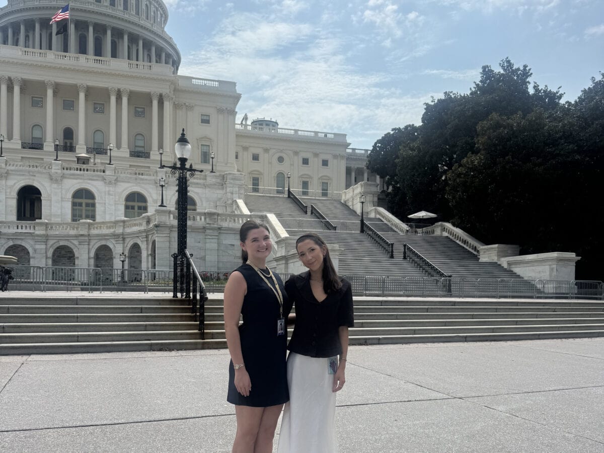 Two young women pose for a photo in front of the capitol building.