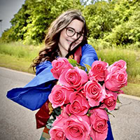 A young women smiles at the camera while holding a bouquet of flowers.