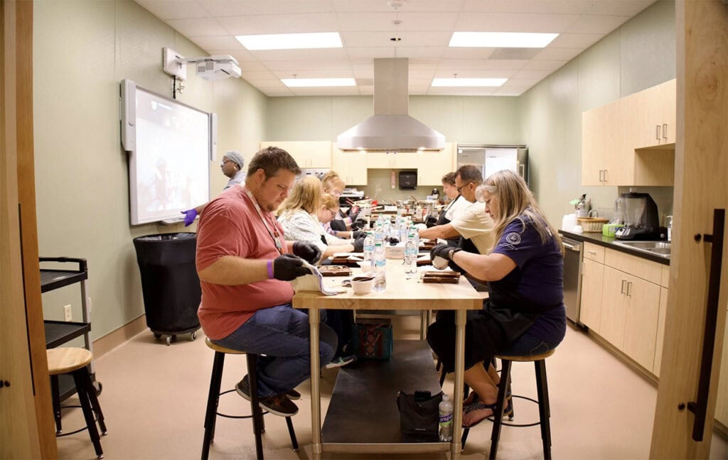 A group of people sit at a table making indigenous food.