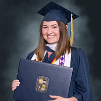 A woman poses for the camera wearing a graduation robe.