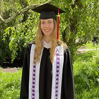 A woman poses for the camera wearing a graduation robe.