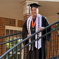 A women poses for the camera wearing a graduation robe.