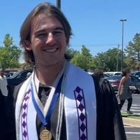 A man poses for the camera wearing a graduation robe.