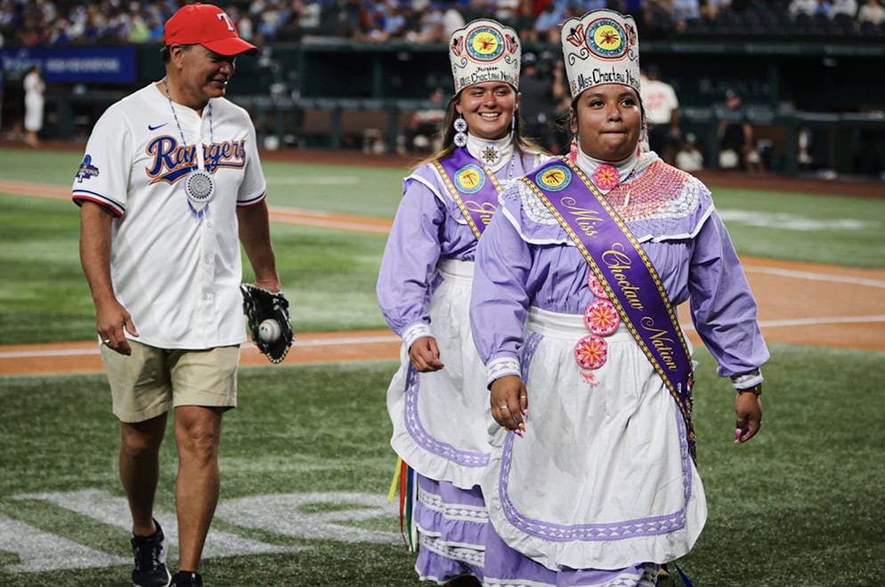 A man walsk alongside two women dressed in traditional Choctaw regalia.