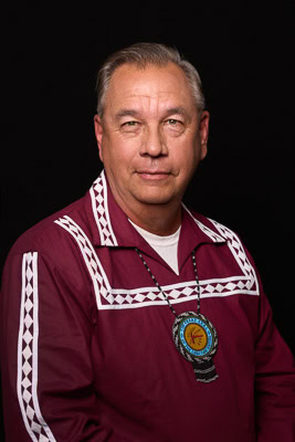 Jess Henry poes for a photo wearing a maroon and white traditional Choctaw shirt.