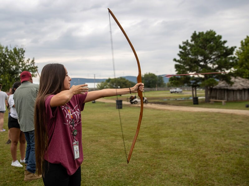 A woman draws back on a bow.