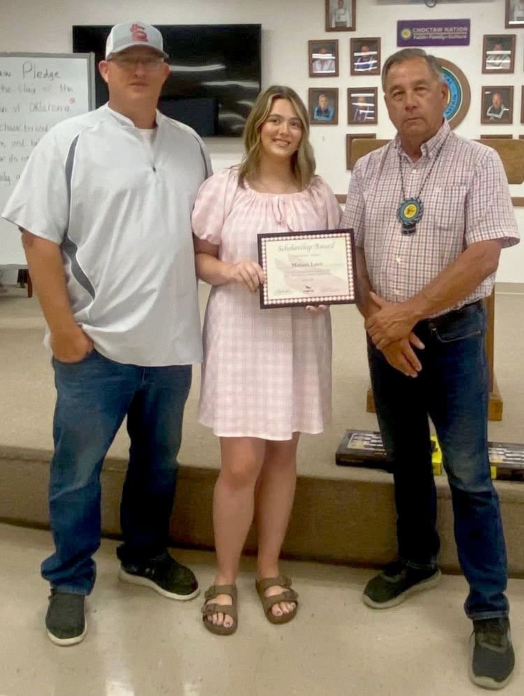 Three people stand, with the middle person holding a certificate.