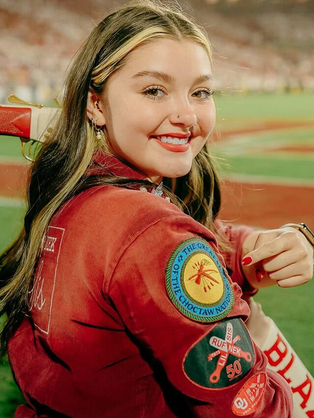 A young woman points to a Choctaw Nation patch on her sleeve.