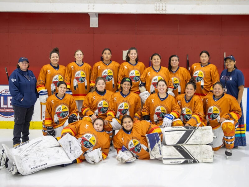 A women's hockey team pose for a group photo on the rink.
