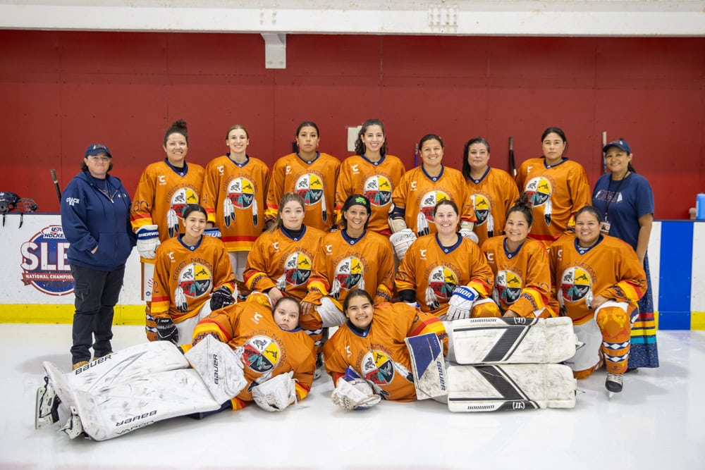 A women's hockey team pose for a group photo on the rink.