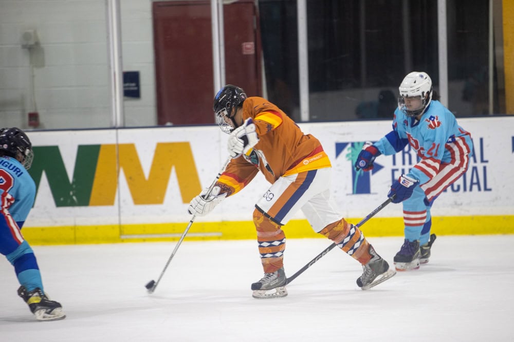 A hockey player in an orange uniform passes the puck on the ice.