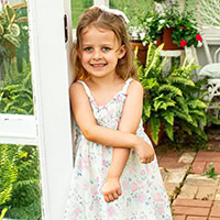 Little girl leans against white door of a greenhouse.