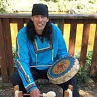 man hold drum, wearing traditional choctaw shirt.