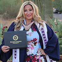 Woman, wearing Choctaw graduation stole, holds up diploma.