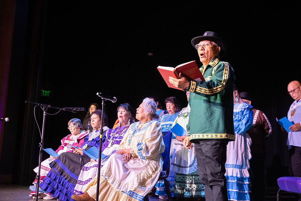 A man holds a hymn book while others behind him sing along.