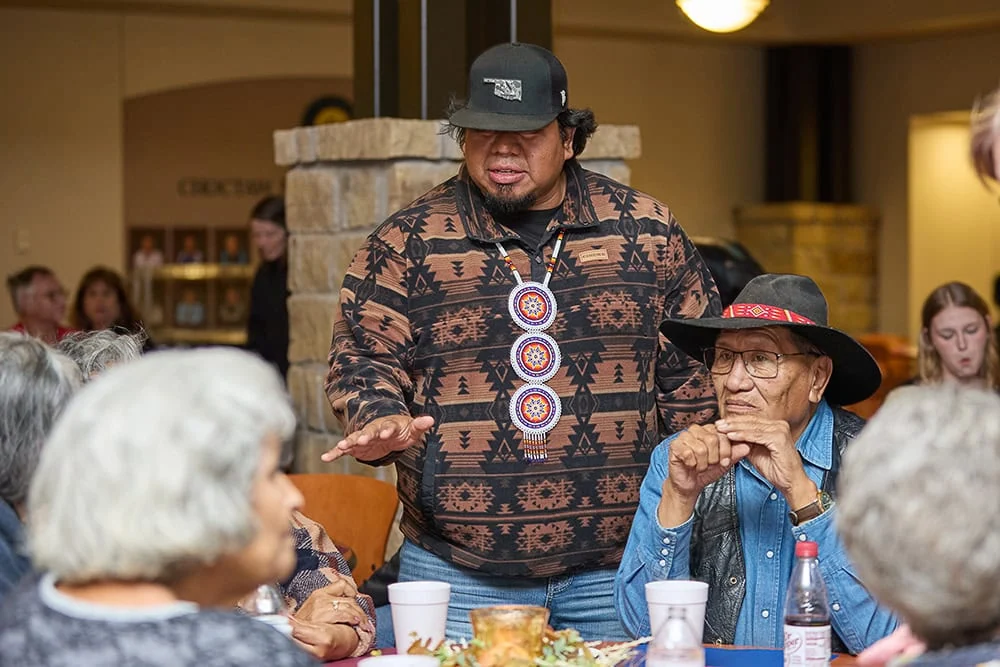A man speaks to a group of people at a table eating.
