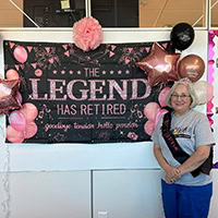 Brenda Ramsey stands in front of a sign that says "the Legend has Retired."