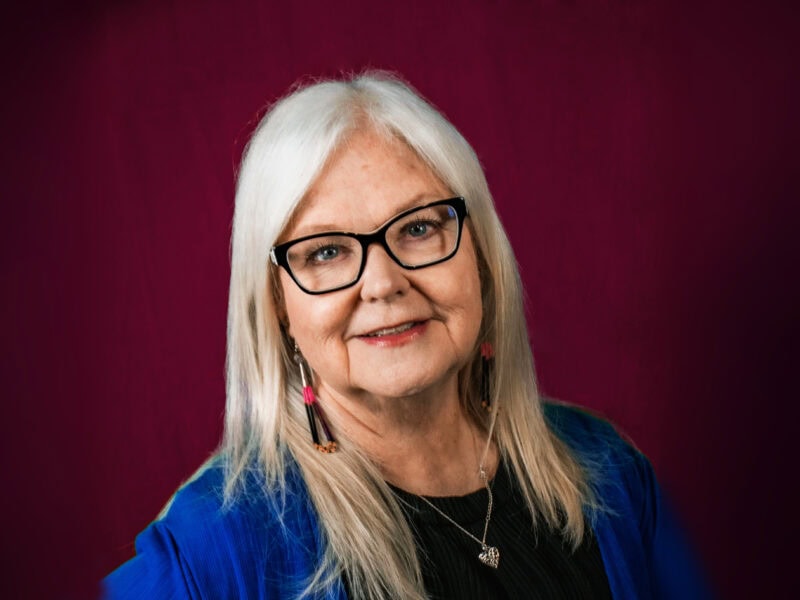 Woman wearing glasses poses for photo in front of maroon background.