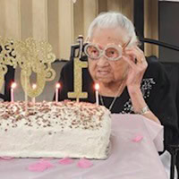 Gladys sockey wears "100" glasses as she blows out candles on her 100th birthday cake