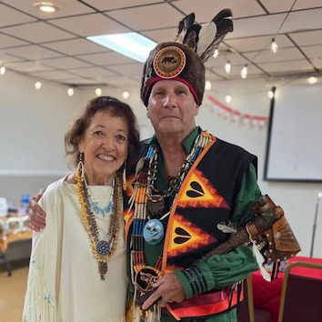 two people in Indigenous regalia pose for a pgoto.