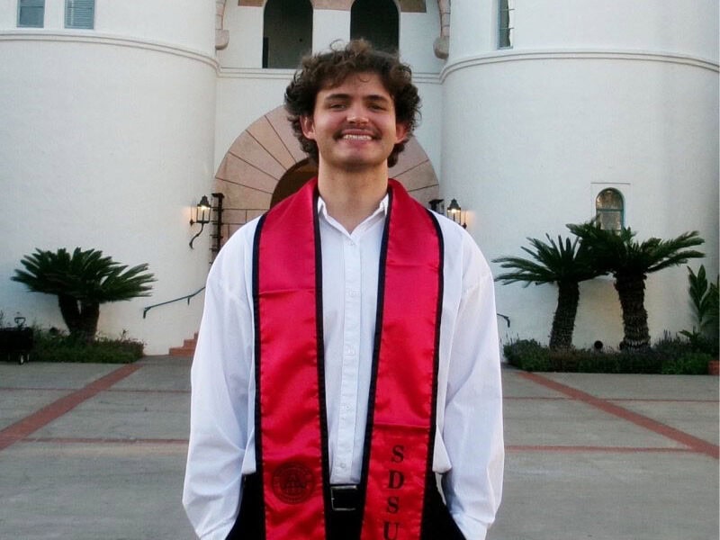 Young man poses for photo with red graduation stole around his neck.