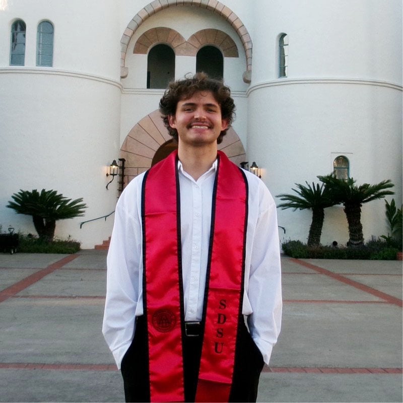 Young man poses for photo with red graduation stole around his neck. 